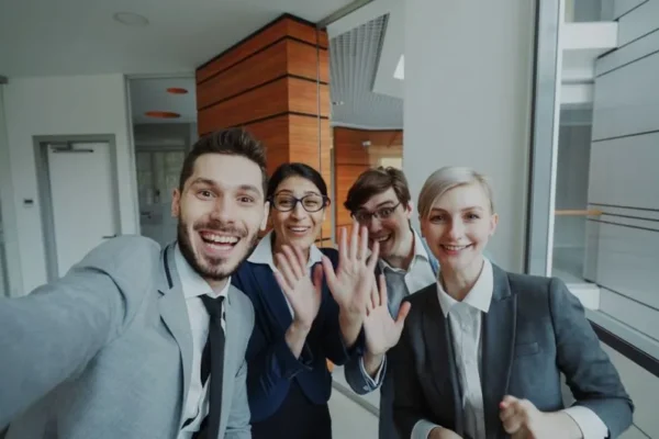 Cheerful business team smiling and waving at the camera indoors.